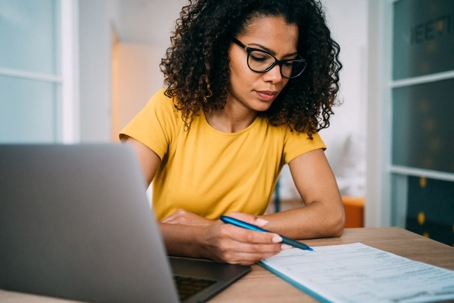 businesswoman using laptop and making notes on a clipboard