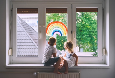 Cute little children on background of painting rainbow on window.