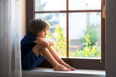Sad child, boy, sitting on a window shield, watching the sunset